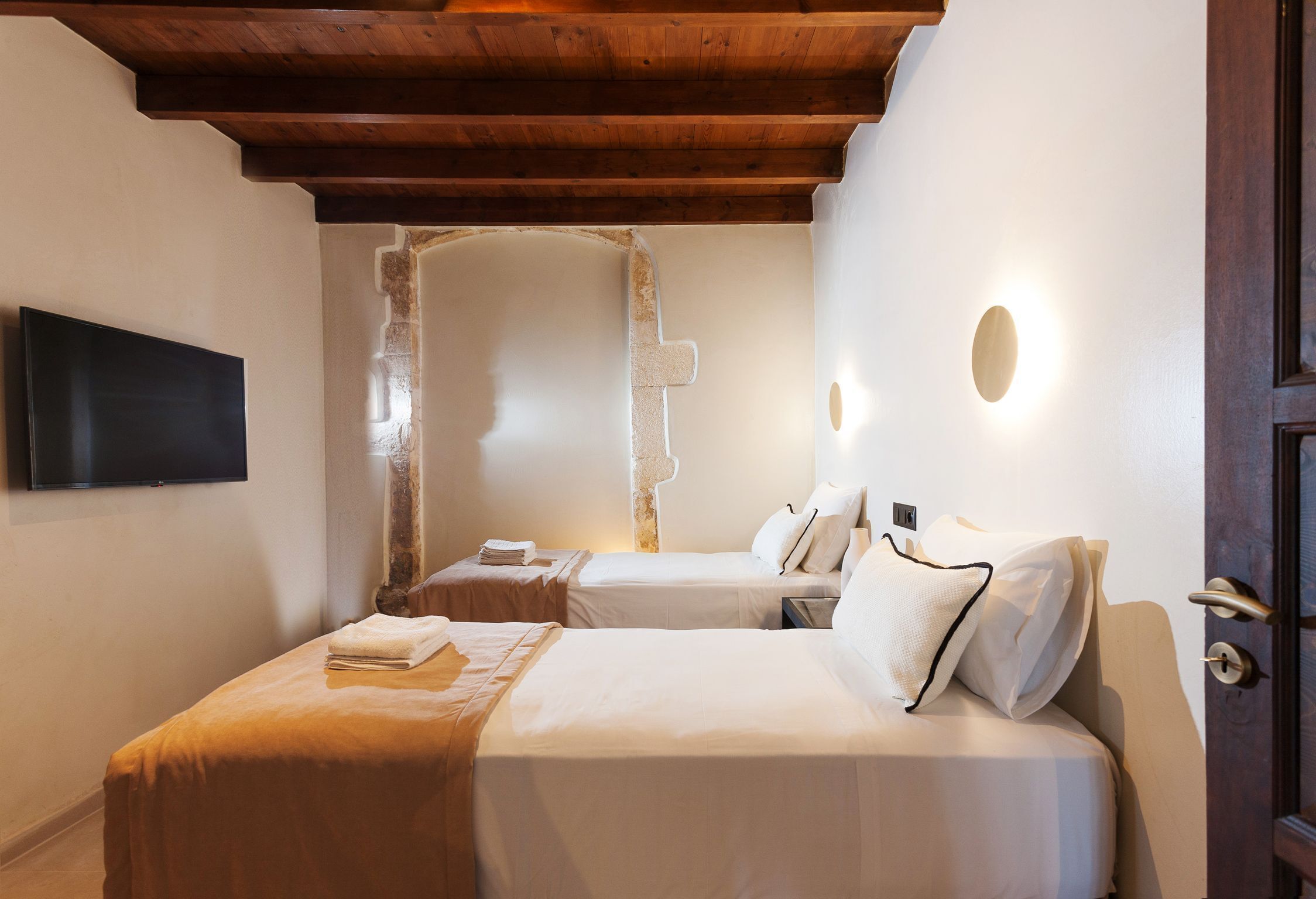 Une chambre d’hôtel avec deux lits, un plafond en bois, un mur en pierre et un téléviseur à écran plat.