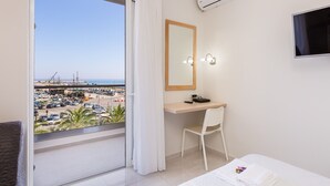 A hotel room with a balcony, a desk, a chair, a bed, and a TV.