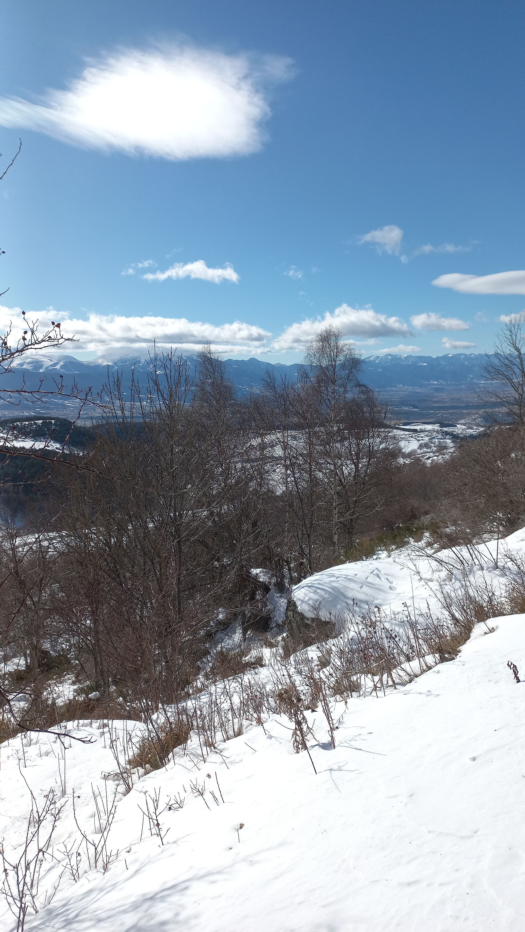 A snowy landscape with mountains in the distance and a clear blue sky.