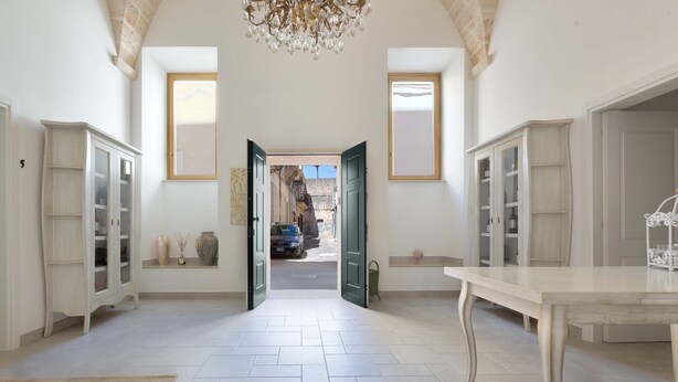 Un vaste hall d’entrée avec un plafond haut, un lustre et une vue sur la rue grâce à des portes ouvertes.