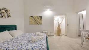 Une chambre d’hôtel avec un lit, des murs blancs, une œuvre d’art en marbre, un vase et une porte.