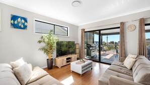 Un salon moderne avec un téléviseur à écran plat, une grande plante en pot, une table basse en bois et un canapé.