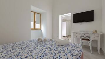 A bedroom with a bed, a desk, a chair, a TV, and a window.