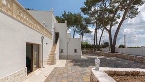 Eine moderne Villa mit einem steinernen Weg, der zu einer Holztür führt, umgeben von einem angelegten Garten und einem weißen Gebäude mit einem Balkon.