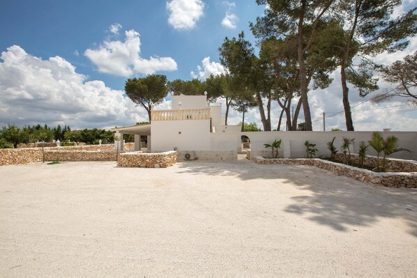 Una casa moderna con un amplio espacio exterior, muros de piedra y árboles altos.