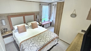Quarto com cama, mesas de cabeceira, cômoda, janela com cortinas e placa fixada na parede.
