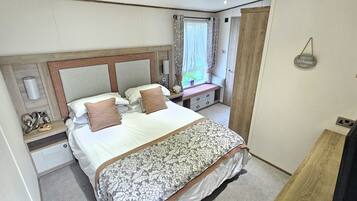 A bedroom with a bed, bedside tables, a dresser, a window with curtains, and a wall-mounted sign.