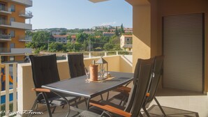 A balcony with a table and chairs, overlooking a residential area with buildings and greenery. - Apartment Sleeps 4 With Sea View (Rijeka)