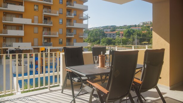 A balcony with a table and chairs, overlooking a yellow building and a pool. - Apartment Sleeps 4 With Sea View (Rijeka)