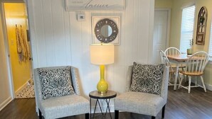 A living room with two armchairs, a small table, a lamp, a patterned rug, and a dining area with a table and chairs.