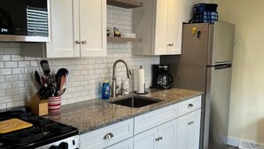 A kitchen with white cabinets, a stainless steel refrigerator, a stove, and a sink.