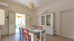 Een eetgedeelte met een tafel voor vier personen, omringd door kleurrijke stoelen, een kast met glazen deuren en een hanglamp.