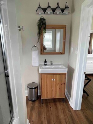 A bathroom with a wooden vanity, a mirror, a sink, and a trash can. - Charming Farmhouse, entire home (Monaca)