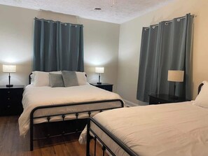A bedroom with two beds, a nightstand with a lamp, and a window with curtains. - Charming Farmhouse, entire home (Monaca)