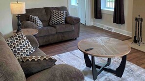 Uma sala de estar com sofá, mesa de centro, luminária, quadro e porta que dá para outro cômodo.
