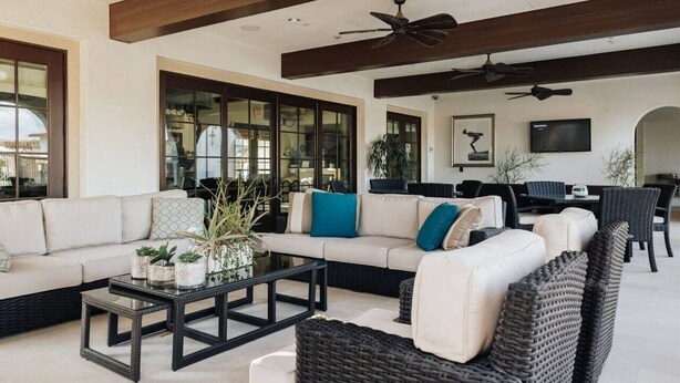 A spacious living area with a sofa set, coffee table, and wicker furniture. There are ceiling fans, a television, and large windows. - Mountain view townhouse w/ fire pit & pool (La Quinta)