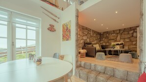 Een eetgedeelte met een ronde tafel en stoelen, een stenen muur en een zithoek met een bank en voetenbank.