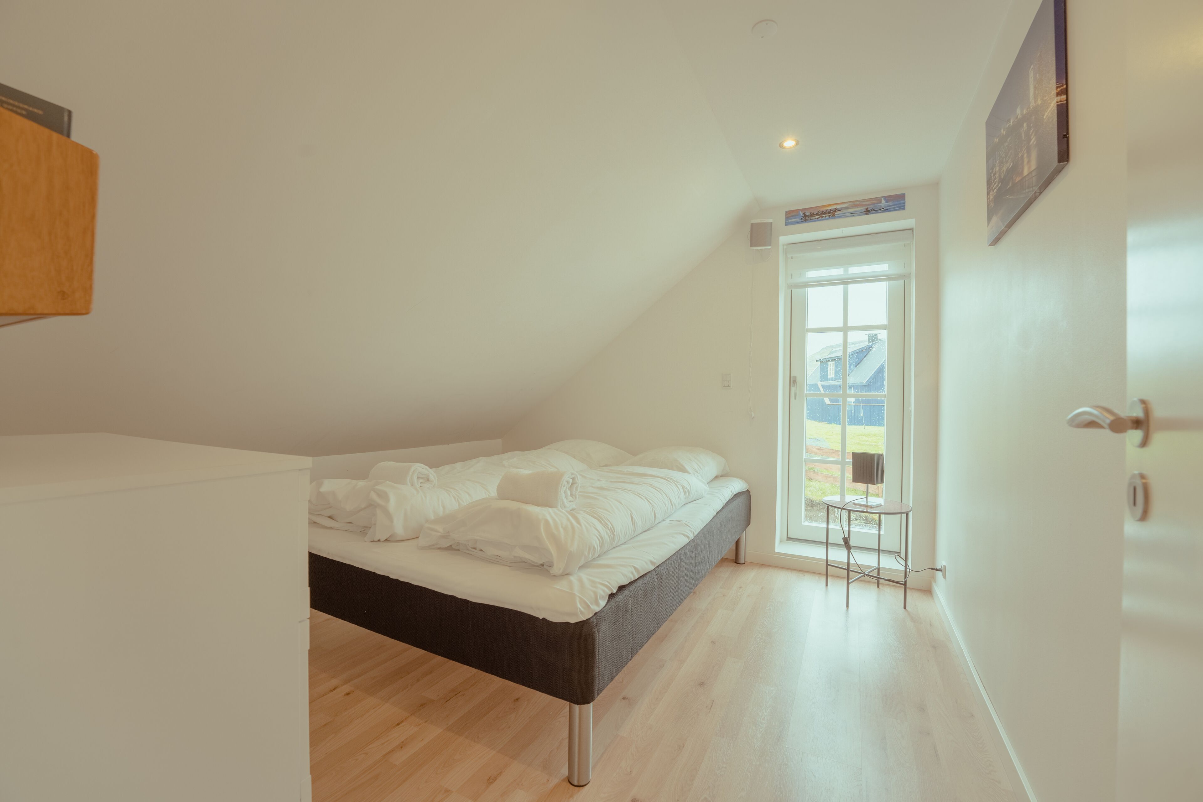 A bedroom with a bed, a small table, and a door leading to a balcony.