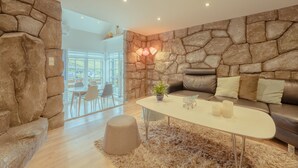 Een moderne woonkamer met een stenen muur, een leren bank, een witte salontafel en uitzicht op de omgeving.