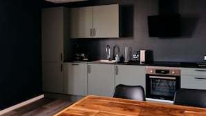 A modern kitchen with grey cabinets, a wooden dining table, and a built-in oven. - Studio Apartment | Unique Location | Stunning View (Hoyvík)