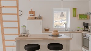 A modern kitchen with a wooden island, two stools, a hanging light, and a view of the outdoors. - Waterfront Retreat | 2 Br Boathouse (Oyrareingir)