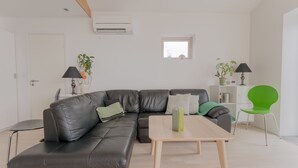 A modern living room with a black leather sofa, a wooden coffee table, and a green chair. There is a small window with a view of the outside. - Waterfront Retreat | 2 Br Boathouse (Oyrareingir)