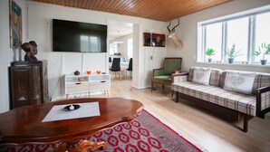 A living room with a wooden ceiling, a plaid sofa, a wooden coffee table, a TV mounted on the wall, and a deer head decoration. - Charming 2Br Apartment, Sea View (Argir)