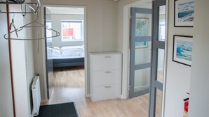 A narrow hallway with wooden flooring, a radiator, a black mat, a bed in the background, and a door leading to another room. - Charming 2Br Apartment, Sea View (Argir)