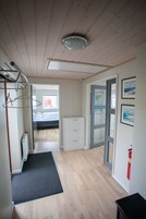 A narrow hallway with wooden flooring, a radiator, a black mat, a bed in the background, and a door leading to another room.