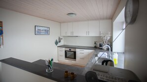 A modern kitchen with white cabinets, a built-in oven, and a large window. - Charming 2Br Apartment, Sea View (Argir)