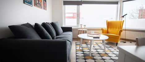 A modern living room with a dark sofa, a yellow armchair, a round coffee table, and a patterned rug.
