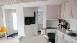 A modern kitchen with a central island, white cabinetry, and a flat-screen TV mounted above the counter. - Hyggeligt | Nordens Hus | Bager | Svartifossur (Tórshavn)