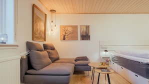 A modern, compact room with a grey sectional sofa, a small round table, and a bed with a white mattress. - Studio Apartment| 20Min From City Center| Tórshavn (Tórshavn)