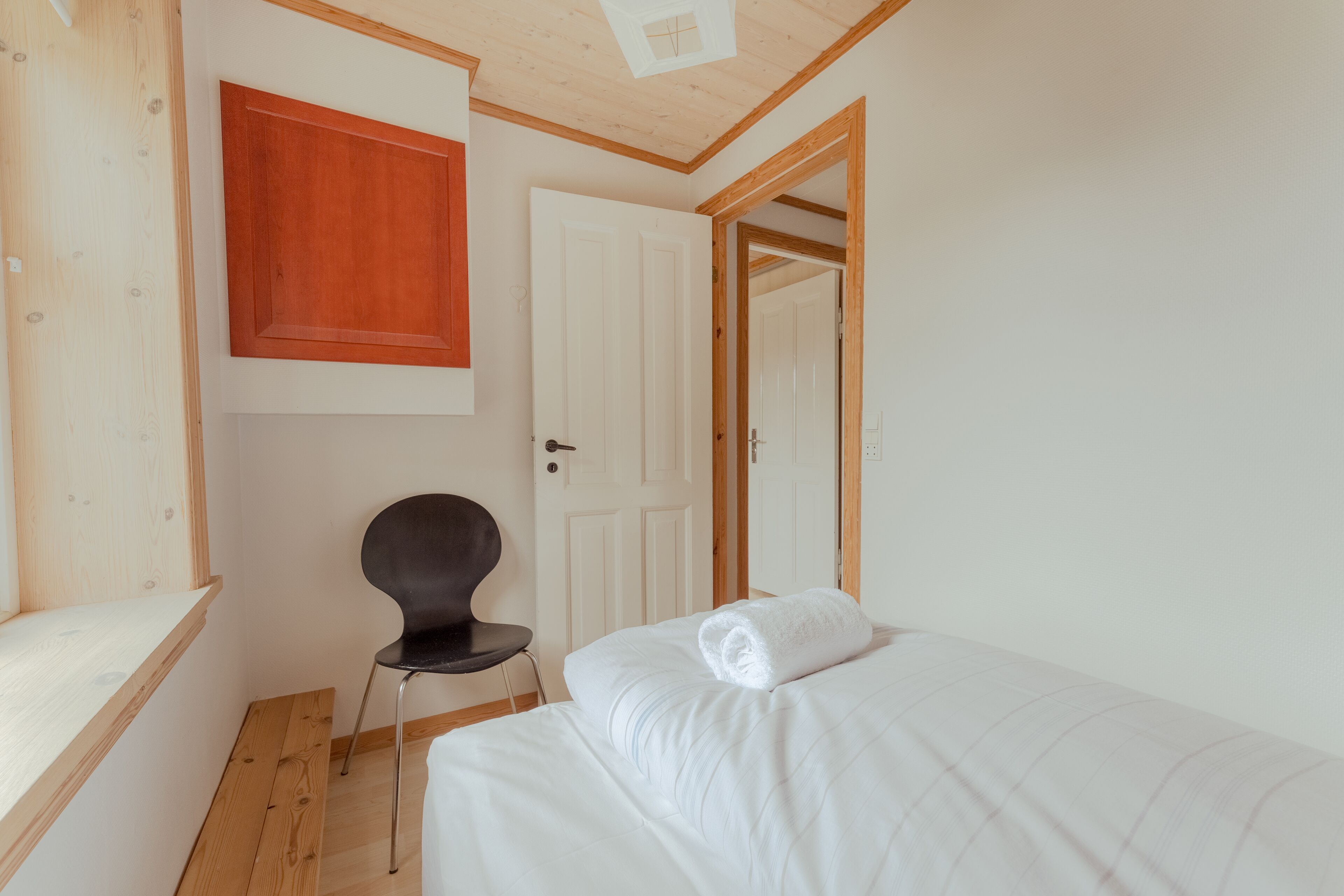 A bedroom with a bed, a chair, a wooden cabinet, and a door.