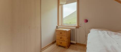 A bedroom with a wooden dresser, a radiator, a window with a view of a green landscape, and a bed.
