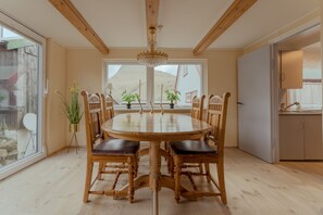 Un coin repas avec une table ronde en bois et des chaises, un lustre et des plantes en pot.