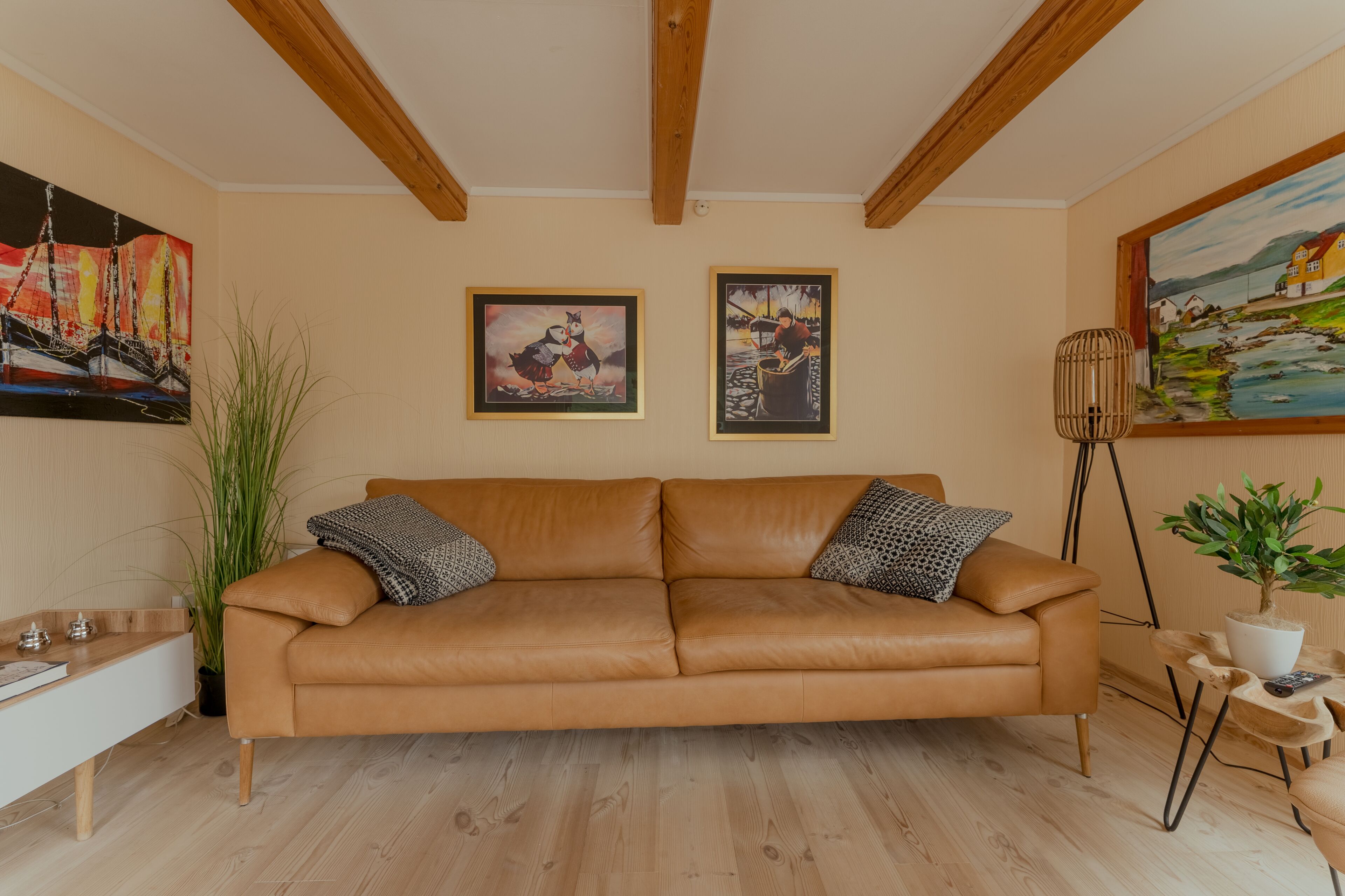 A tan leather sofa with patterned cushions, a wooden floor, and artwork on the walls.