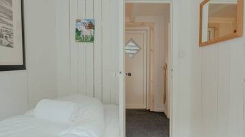 Une pièce avec un lit, une porte donnant sur une autre pièce, un tableau encadré au mur et un miroir sur le côté droit.