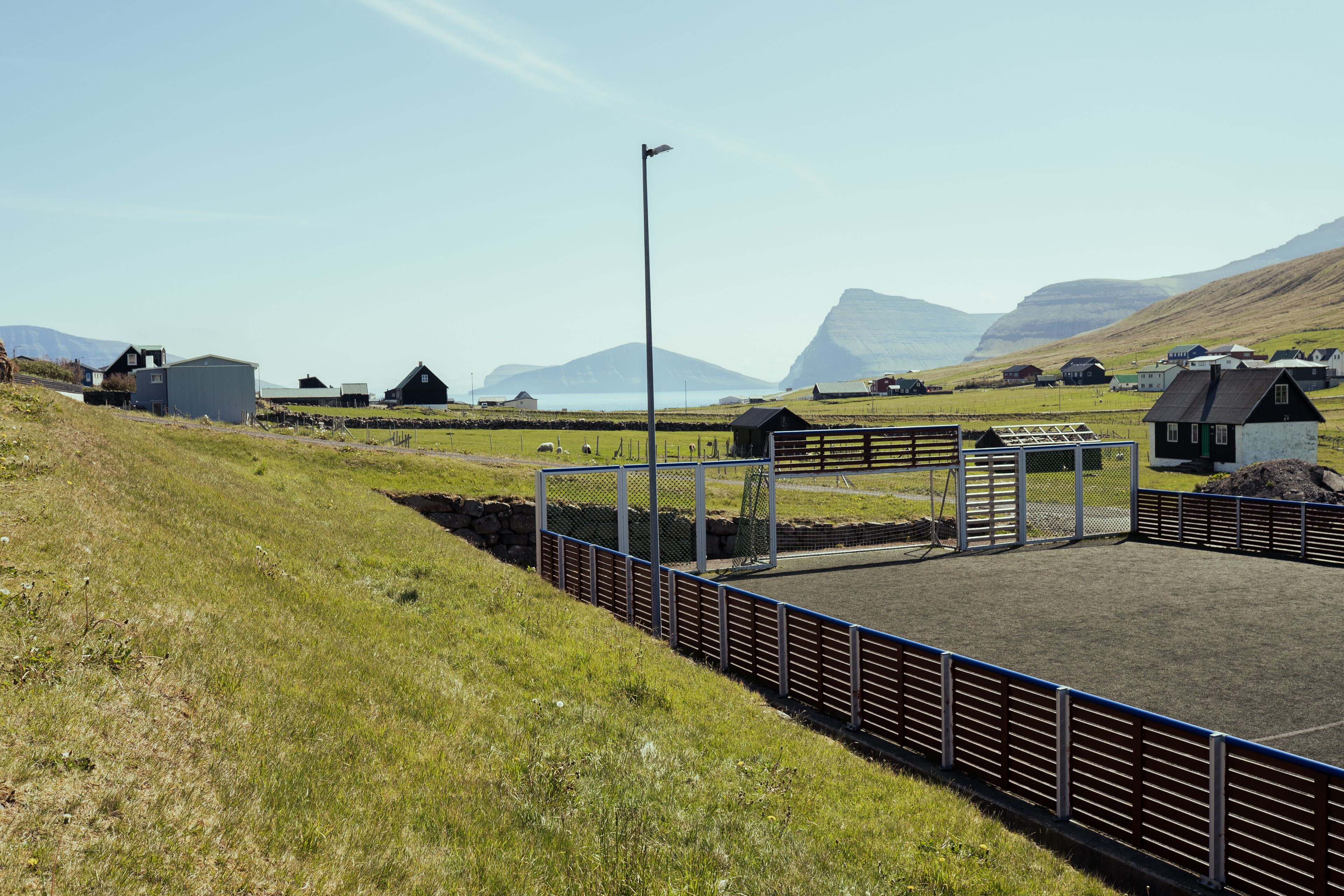 Ländliche Landschaft mit einem eingezäunten Bereich, Gebäuden und einem Berg im Hintergrund.