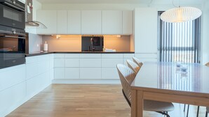 A modern kitchen with white cabinetry, a built-in oven, and a dining area with a wooden table and chairs. - Stunning Sea View | 1 Bedroom Apartment | Tórshavn (Tórshavn)