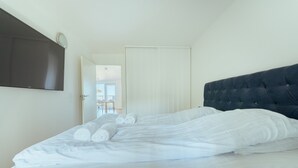A neatly made bed with white linens and rolled towels, a dark upholstered headboard, and a flat-screen TV mounted on the wall. - Stunning Sea View | 1 Bedroom Apartment | Tórshavn (Tórshavn)