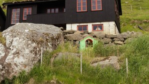 Un bâtiment noir avec des fenêtres rouges et une porte verte, entouré de rochers et d’herbe.
