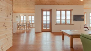 Une pièce spacieuse avec un plancher et des murs en bois, une grande table en bois et une vue sur l’extérieur, visible à travers une porte.