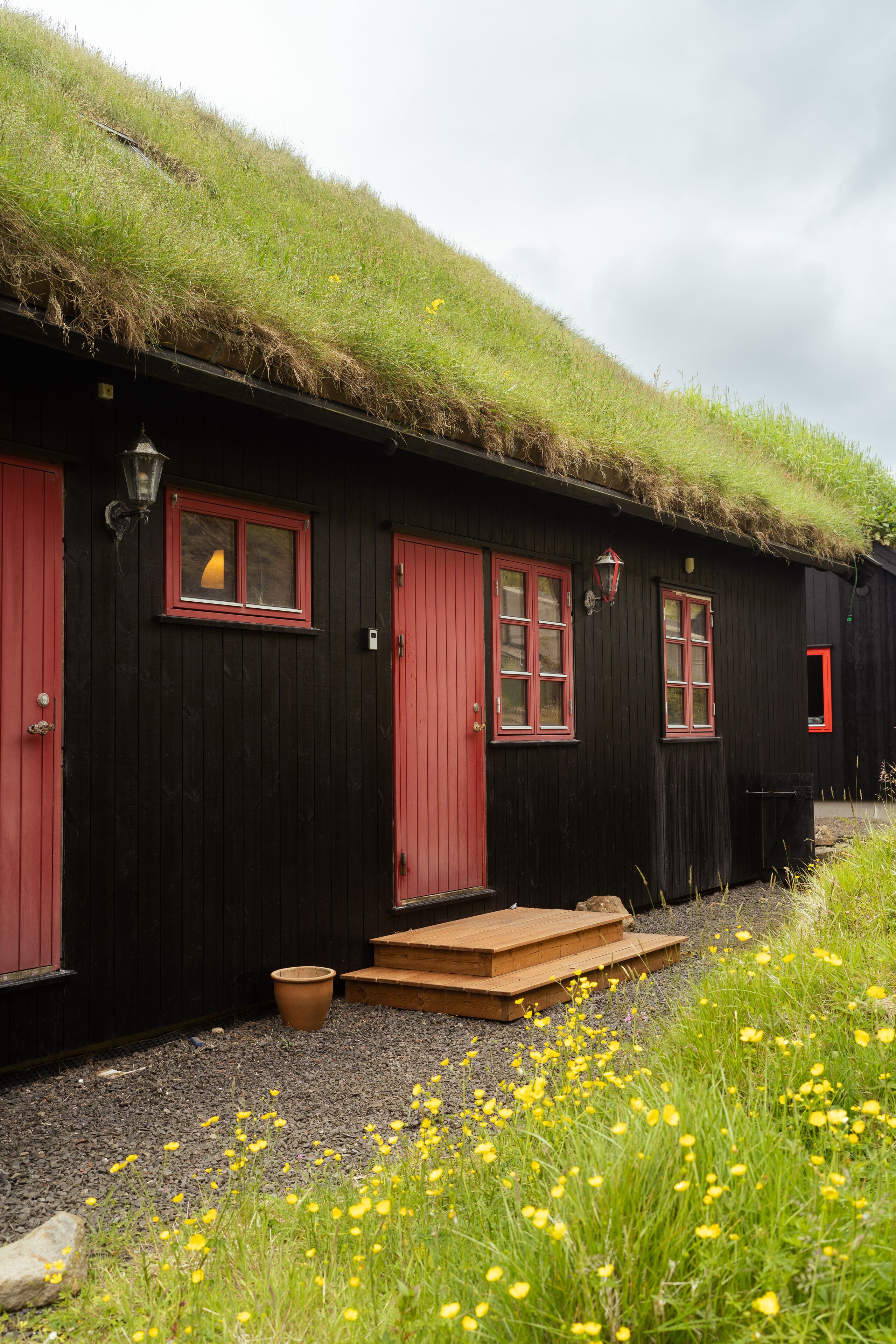 A black wooden building with red doors and windows, a thatched roof, and a gravel path leading to the entrance.