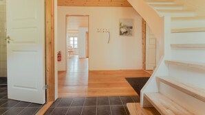 Un couloir au plancher en bois, un escalier aux marches blanches et un luminaire au plafond.
