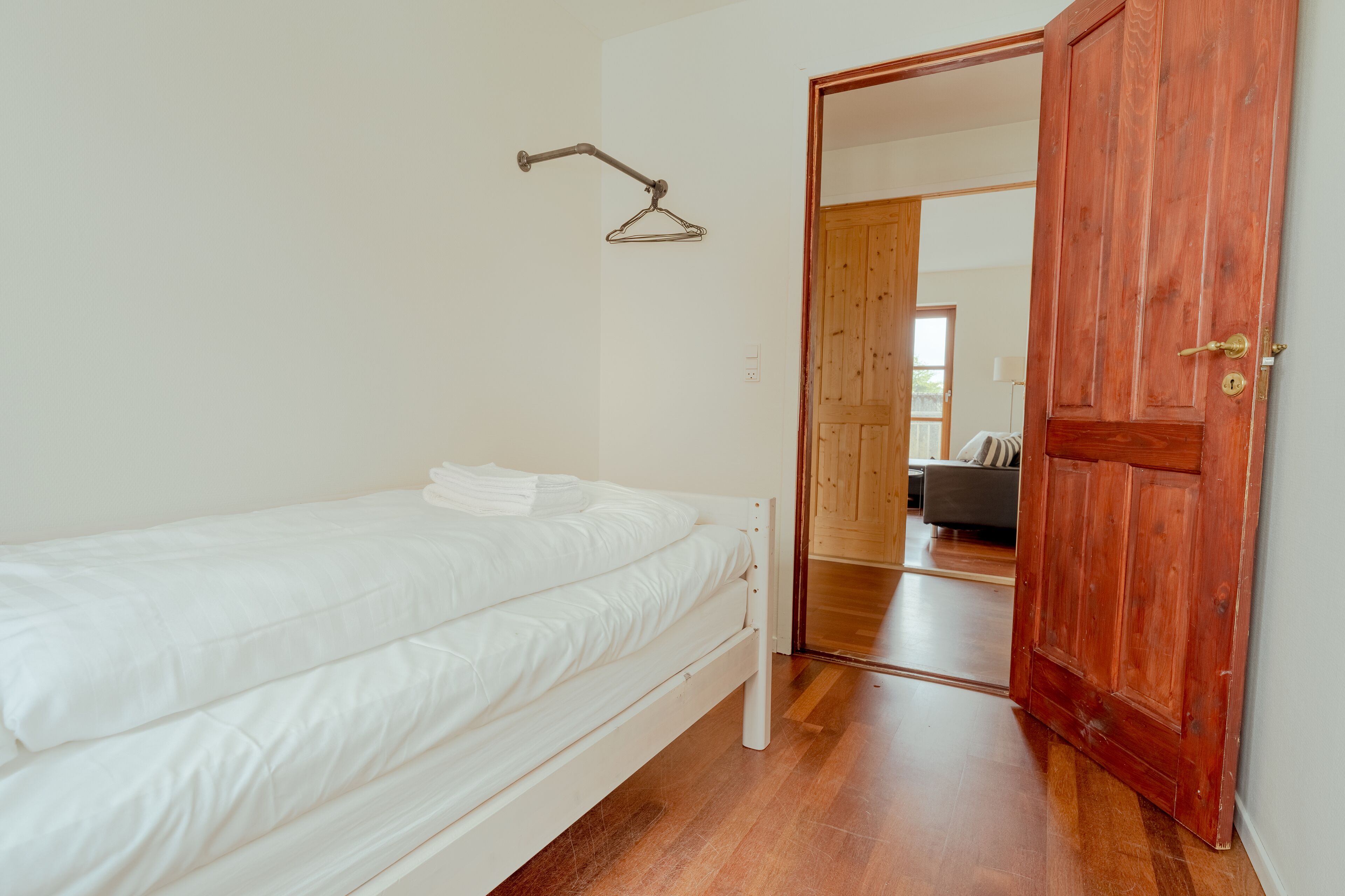 Un dormitorio con una cama individual, una puerta de madera y un pasillo que conduce a otra habitación.
