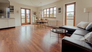 A spacious living room with a sofa, a dining table with chairs, and a kitchen area with cabinets and a refrigerator. - Marina View |3 Bedroom Apartment |Central Tórshavn (Tórshavn)