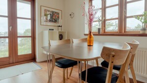 A dining area with a wooden table, black cushioned chairs, a vase with pink flowers, and a painting on the wall. - Marina View |3 Bedroom Apartment |Central Tórshavn (Tórshavn)