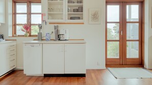A modern kitchen with white cabinetry, a dishwasher, a coffee maker, and a window with a view of the outside. - Marina View |3 Bedroom Apartment |Central Tórshavn (Tórshavn)