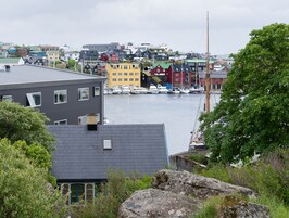 Un pueblo costero con edificios coloridos, un puerto deportivo con barcos y una gran roca en primer plano.